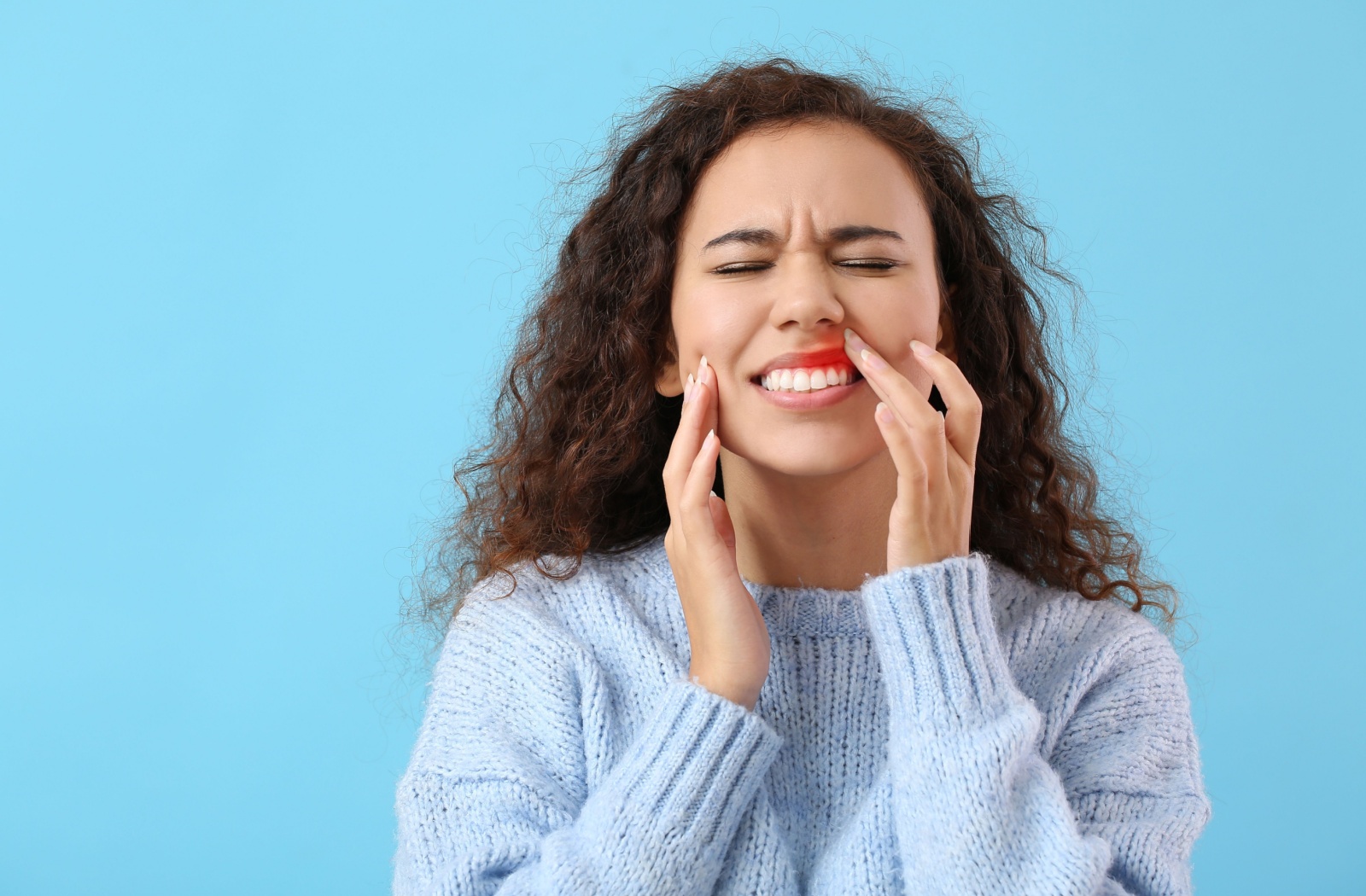 Woman in a light blue sweater grimacing in pain while holding her jaw highlighting gum pain or periodontal disease