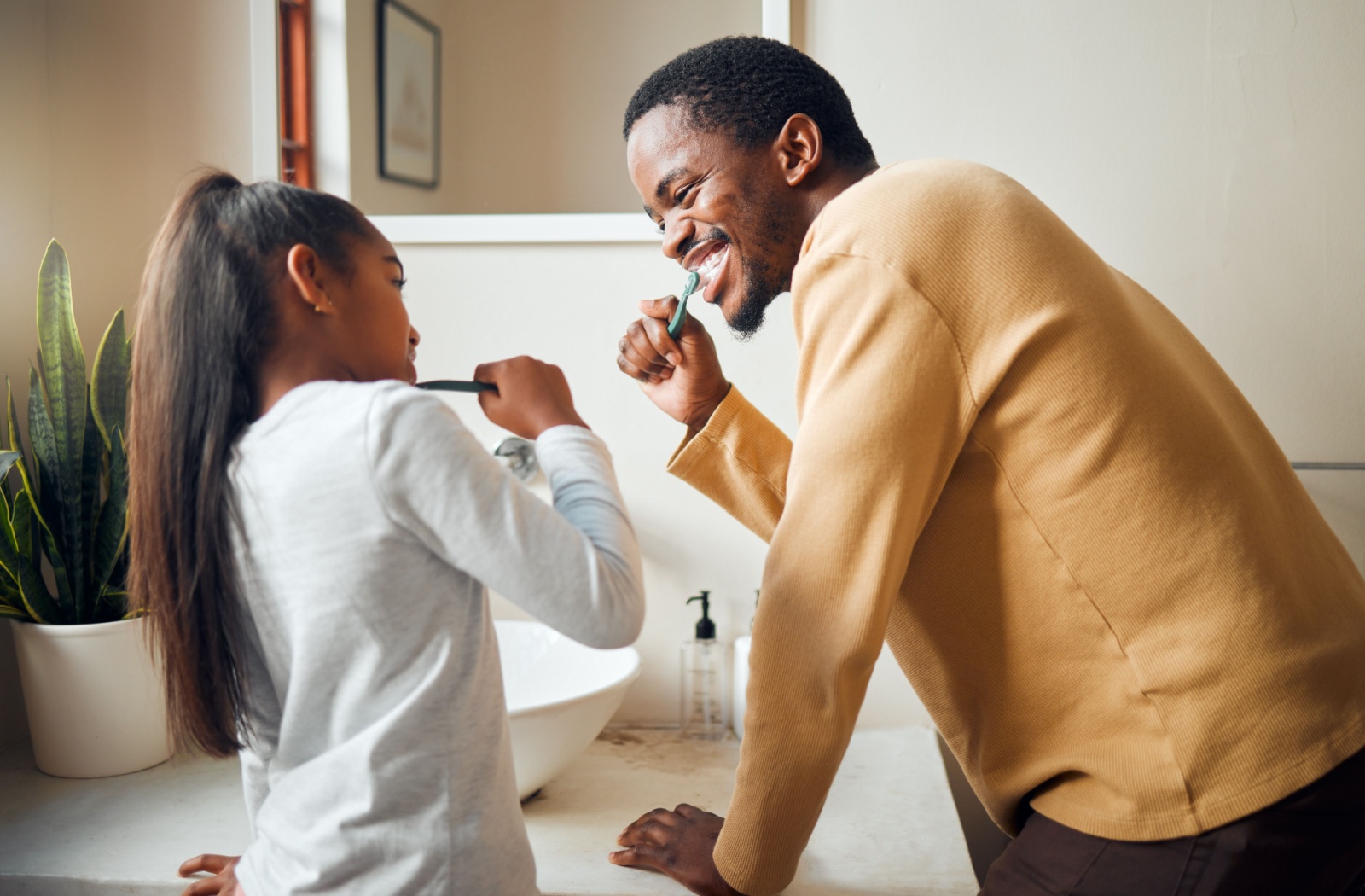 A child and their parent brushing their teeth together with fluoride-free toothpaste.