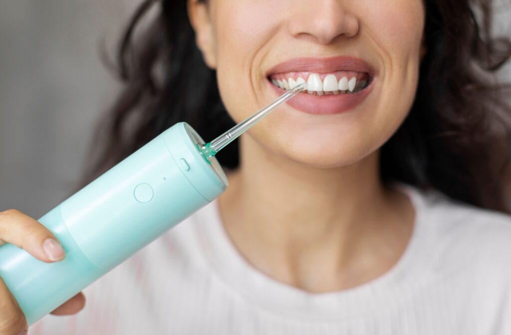 A close up photo of a person using a water flosser to floss their teeth.