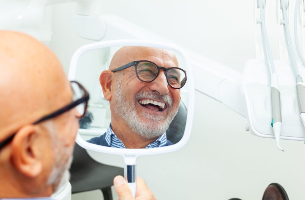 Older adult laughing at their reflection in hand-held mirror at a dental clinic.