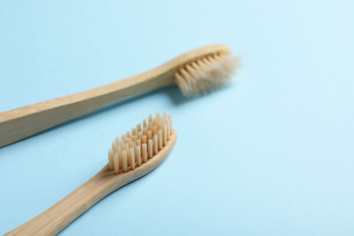 Comparison of worn bamboo toothbrush with frayed bristles next to new toothbrush with fresh intact bristles on blue background.